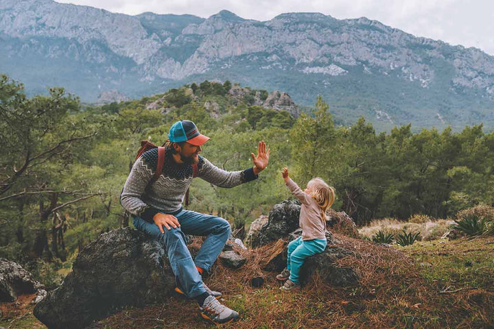 Father and toddler daughter high-five hands while sitting in the mountains. 