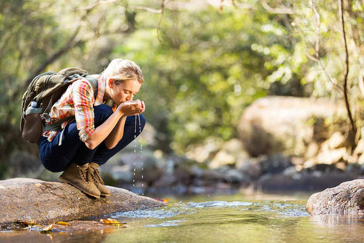 A hiker drinking from a stream